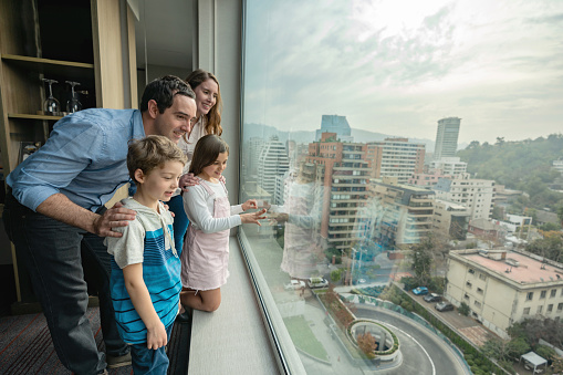 Excited family of four at their hotel bedroom looking at a beautiful window view all smiling very happy
