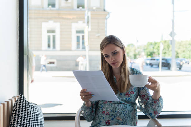 istock Woman sits, drinks coffee, and reads documents by large window 1167109502