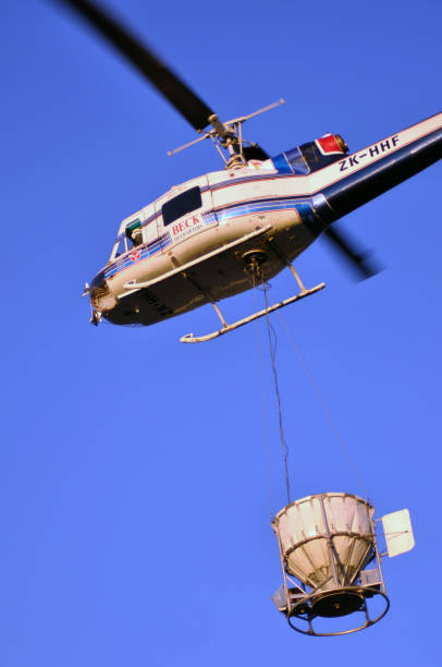 helicopter taking off Greymouth, New Zealand, circa 2009: Iroquois helicopter takes off with a load of 1080 pellets in a monsoon bucket. The 1080 pellets are a controversial method of controlling possums in New Zealand's native bush. possum nz stock pictures, royalty-free photos & images