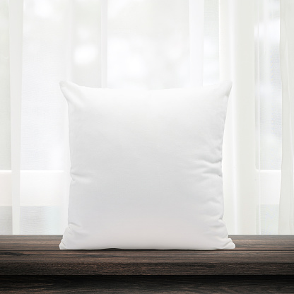 Blank pillows made from soft feather on morning window and curtains background with bedding concept. White pillow template place on wooden table for your design.