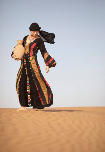 middle aged woman in yemeni traditional dress in a desert with a water dish