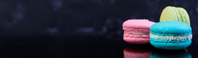 Delicious colorful macaron cakes on dark background. Banner.