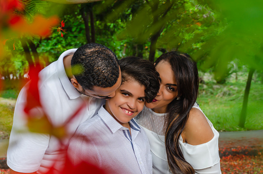 couple of Latin American men and women, with
boy suffers autism, happy in a portrait
family outdoors together in a
park, the three laughing hugging