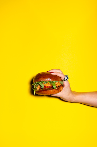 Hand holding burger against yellow background