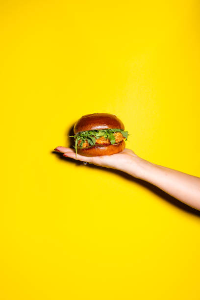 istock Hand holding burger against yellow background 1167149558