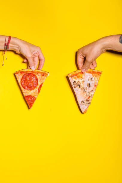istock Two hands holding two slices of pizza against yellow background 1167149592
