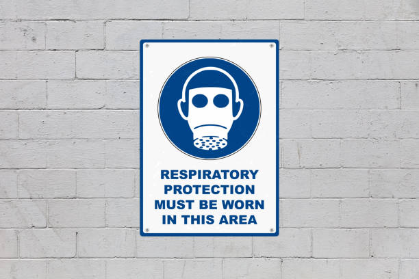 White and blue mandatory sign screwed to a brick wall to warn about a threat. In the middle of the panel, there is a gas mask symbol and the message saying \