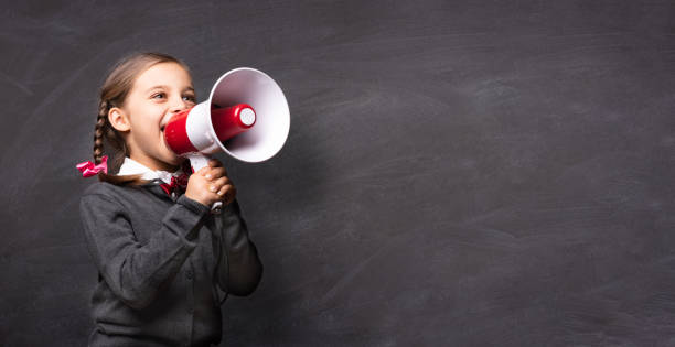 child girl student shouting through megaphone on blackboard backdrop with available copy space. back to school concept. - marketing megaphone child using voice imagens e fotografias de stock