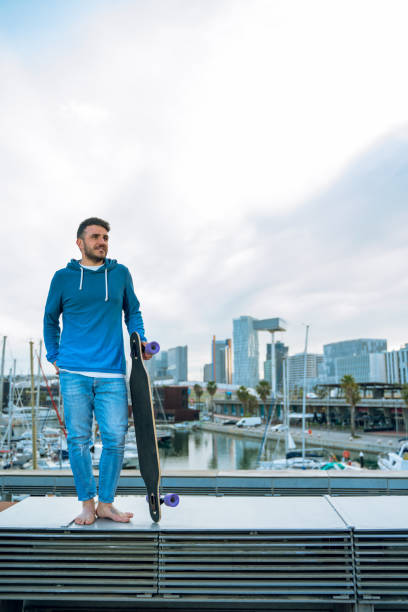 Man standing with his longboard at the port. Barcelona skyline at background stock photo