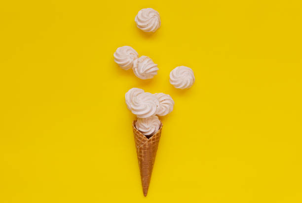 Waffle cone and white twisted meringues on yellow background