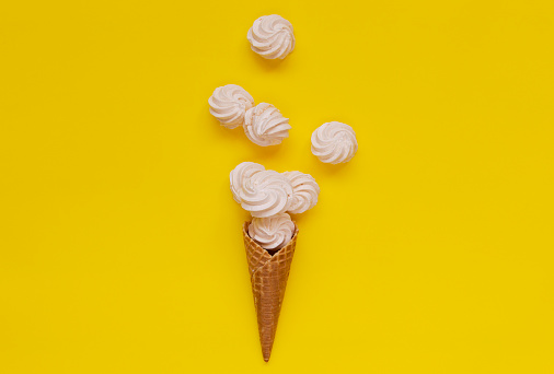 Waffle cone and white twisted meringues on yellow background