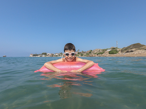Happy boy swimming in the sea on inflatable mattress.
