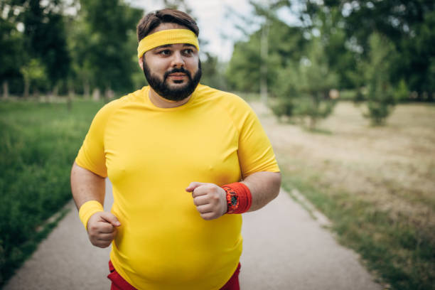 Young large build guy jogging in park One man, young overweight man jogging alone in park. sweat band stock pictures, royalty-free photos & images
