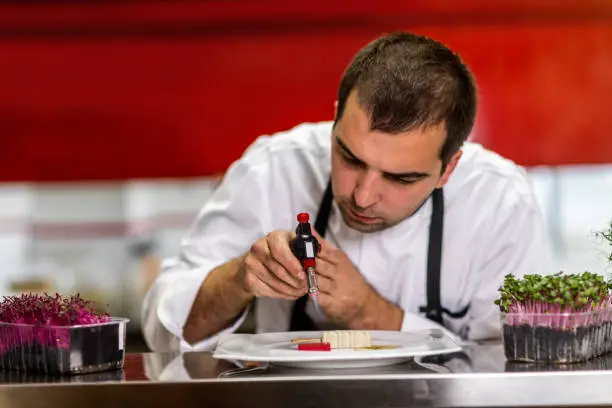 Chef using a kitchen blowtorch to caramelize a molecular cuisine meal in a restaurant kitchen.