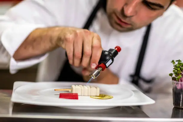 Chef using a small blow torch to add finishing glaze over a molecular cuisine dish.