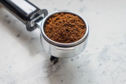 Closeup view of portafilter with ground coffee for coffee machine barista on marble table