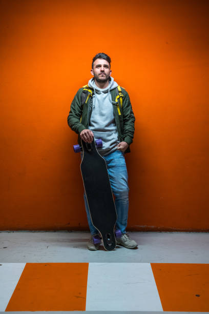 istock Casuan man leaning on an orange wall with his longboard 1167168839