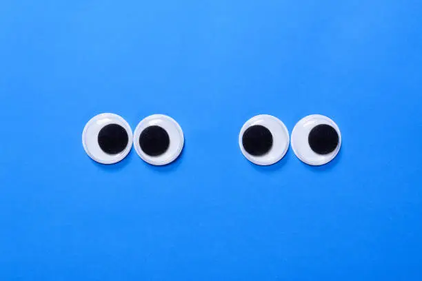 Photo of Googly eyes: Two pair strabismus and squint mad googly eyes next to each other on a blue background.