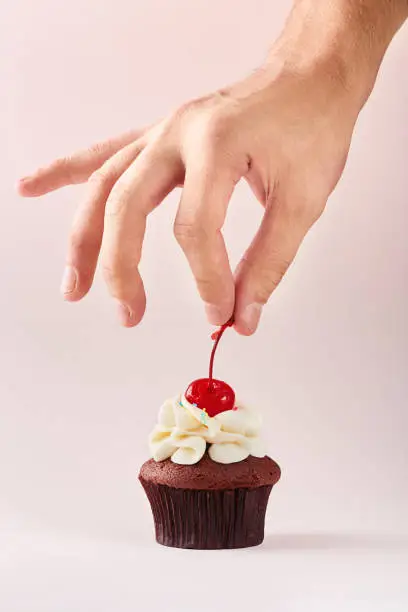 Cupcake decoration. Hand decorating cupcake adding cherry on top.