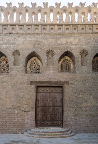 istock Wooden weathered door, perforated stucco window decorated with floral patterns, and three steps on stone bricks wall 1167180899
