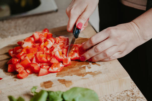 Woman hands cut red tomato Cutting vegetables. Woman's hands with manicure are cutting a knife a red ripe tomato on a square wooden board chop stock pictures, royalty-free photos & images