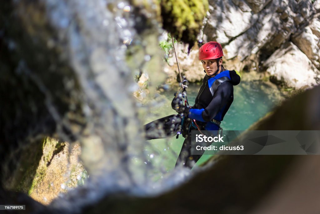 Girl rappelling in the canyon adventure with waterfall and turquoise water in the background Canyoning as one of the most extreme outdoor sports. Canyoneering Stock Photo