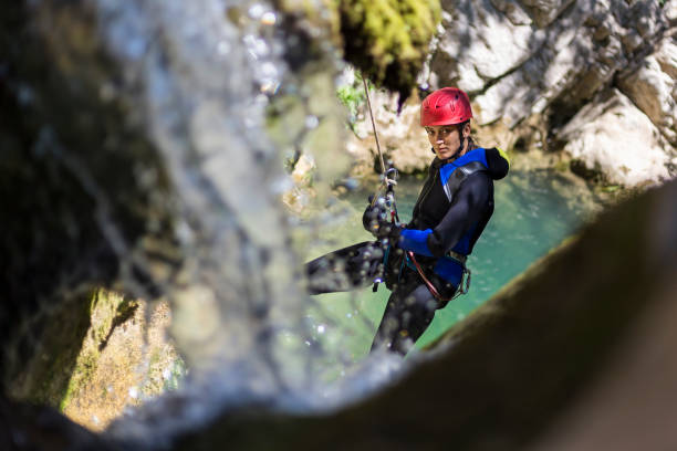Girl rappelling in the canyon adventure with waterfall and turquoise water in the background stock photo