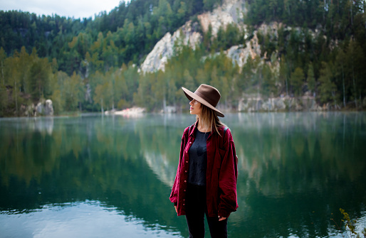 Young woman in hat and red shirt near lake in a mountains.