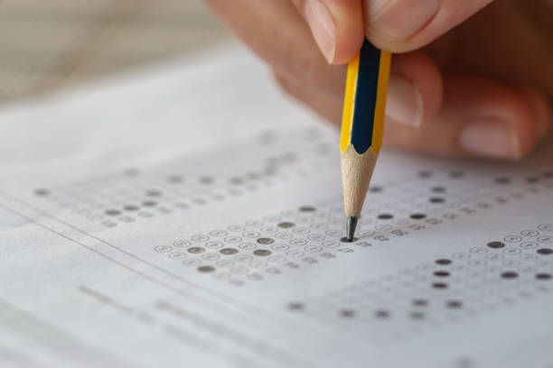 istock School or university students hands taking exams, writing examination room with holding pencil on optical form answers paper sheet on desk doing final test in classroom. Education assessment Concept 1167189640