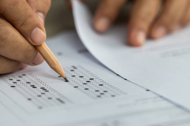 istock Education school test concept : Hands student holding pencil for testing exams writing answer sheet or exercise for taking fill in admission exam multiple carbon paper computer at university classroom 1167189764