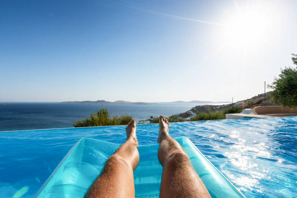 maschio che galleggia sull'acqua blu della piscina con vista sul mare - sea swimming greece women foto e immagini stock