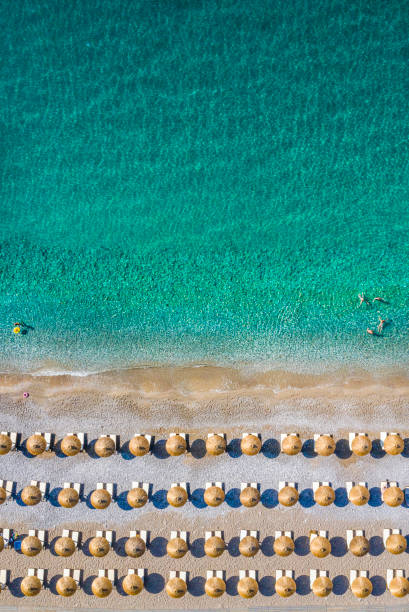 A couple of rows of sunbeds and umbrellas on a beach and an emerald sea, taken from air Rows of beach umbrellas and sunbeds on a beach of an emerald sea, taken from above. beach umbrella aerial stock pictures, royalty-free photos & images