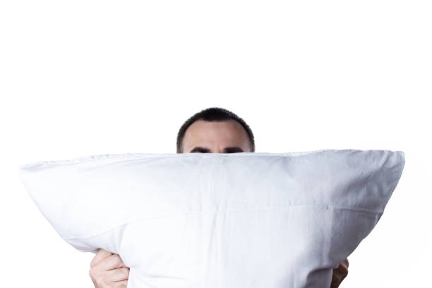 istock Man with pillow isolated on white background. Resting after working day or waking up in the morning. Man hiding her face behind pillow 1167194140