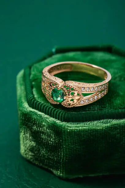 Wedding ring with emerald green gemstone on green velvet jewelry box. Rose gold engagement or proposal ring with gemstone