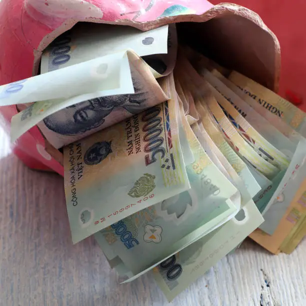 Saving money from broken piggy bank after long time to save up for emergency situation or retirement planning or buy house, many Vietnamese dong banknote on wooden background