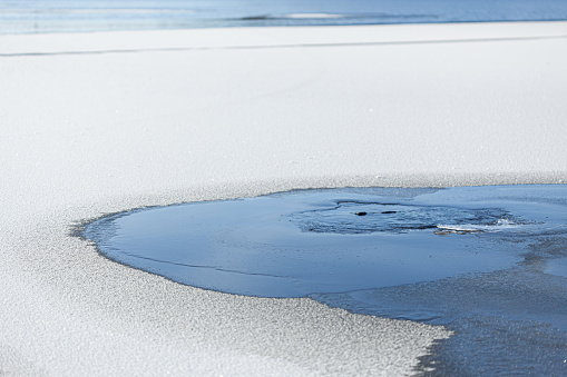 Water coming from hole in frozen lake ice surface