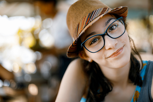 Photo of a pretty young girl wearing eyeglasses and hat looking at the camera. Shot with DSLR Canon Mark IV