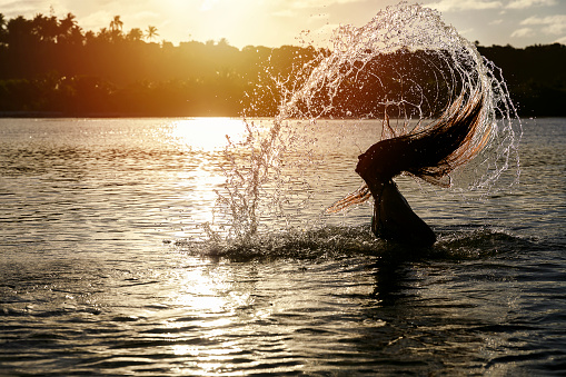 Photo of a woman throwing water up with her hair at sunset. Shot with DSLR Canon Mark IV