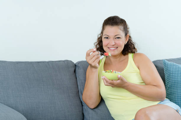 istock Woman sitting on couch eating fruit salad 1167208812