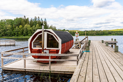 Ullared, Sweden - july 16; 2019: Summer lake landscape view of a traditional scandinavian water floating red wooden sauna next to a jetty at an public recreation area in Ullared Sweden July 16, 2019.