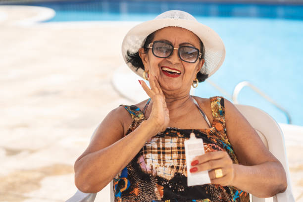 Mature woman applying suntan lotion Sunbathing, Applying, Candid, Sunglasses, Sunlight sun hat stock pictures, royalty-free photos & images