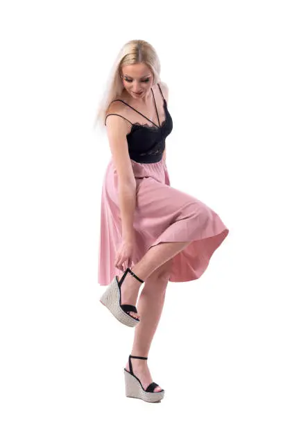 Elegant woman in salmon color skirt adjusting platform sandal shoe strap. Full body isolated on white background.
