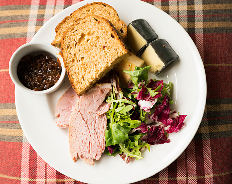 Ham, rustic bread, fig chutney, cheese, rocket salad on a plate sitting on tartan plaid cloth, Scotland, UK