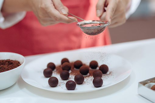 an asian chinese mid adult female dessert chef dusting and coating chocolate truffles in the domestic kitchen