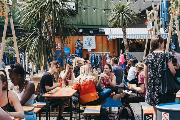 People eating and drinking at the tables inside Pop Brixton, London, UK. London, UK - July 16, 2019: People at the tables inside Pop Brixton, event venue and the home of a community of independent retailers, restaurants, street food startups and social enterprises. brixton stock pictures, royalty-free photos & images