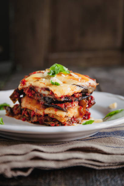 tradicional parmigiana di melanzane: berenjena al horno - italy, sicily cousine. berenjena al horno con queso, tomates y especias en un plato blanco. un plato de berenjena está sobre una mesa de madera - aubergines parmesan fotografías e imágenes de stock