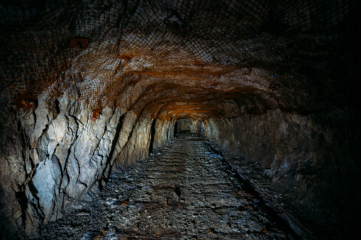 Dark dirty abandoned uranium mine with rusty remnants of railway.
