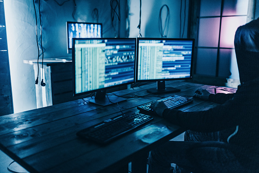 Male programmer working on desktop computer at desk in office in dark