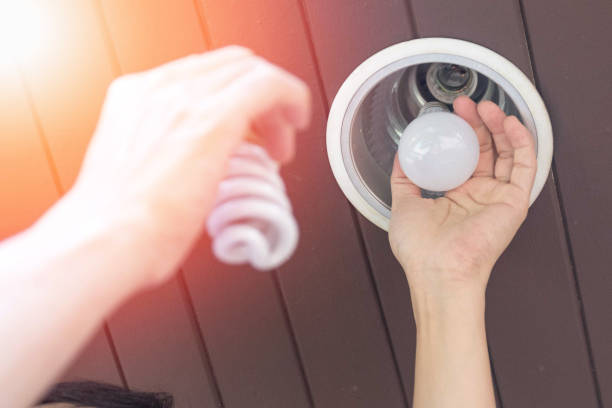 conceito da economia de poder. homem de ásia que muda bulbos compact-fluorescentes (cfl) com a ampola nova do diodo emissor de luz. - lâmpada de poupança de energia - fotografias e filmes do acervo