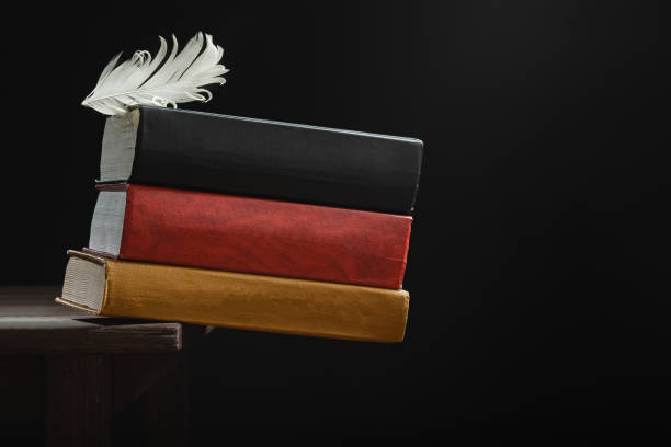 German flag and feather Feather holds a stack of books folded on the edge of the table. Conceptual photo german language photos stock pictures, royalty-free photos & images